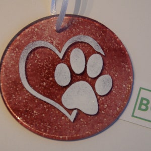 May include: A round, red-brown glass bauble with a white paw print inside a white heart. The bauble has a speckled, textured surface.