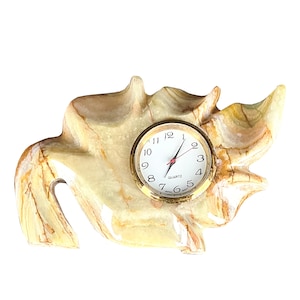 May include: A decorative clock made of light brown and white marble with a gold-colored frame. The clock face is white with black numbers and hands. The clock is shaped like a stylized leaf.