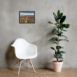 May include: An aerial photograph of a residential neighborhood with houses and trees in autumn colors. The photo is framed in a black frame.