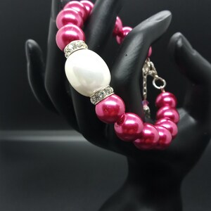 Op de afbeelding: Een roze parel armband met een grote witte parel en strass accenten.