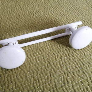 Op de afbeelding: Witte metalen handdoekrek met twee ronde uiteinden. Het rek is ontworpen om aan de muur te worden gemonteerd.