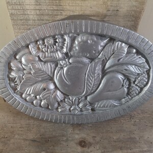 Peut inclure: Un plateau de service ovale en argent avec deux poignées. Le plateau est décoré d'un motif en relief de fruits et de feuilles.