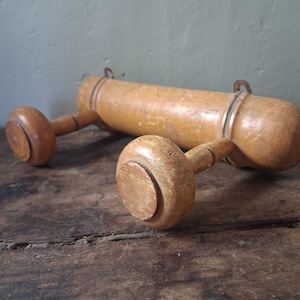 Può includere: Un mattarello vintage in legno con due manici arrotondati e un corpo cilindrico. Il mattarello è realizzato in legno chiaro e presenta anelli e ganci in metallo. Poggia su una superficie di legno scuro.