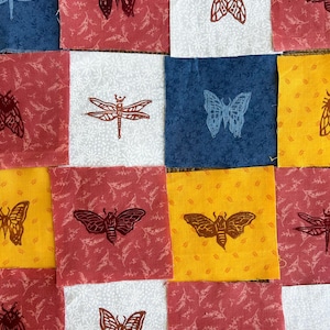 Op de afbeelding: Een verzameling stoffen vierkanten in verschillende kleuren, waaronder rood, blauw, wit en geel. Elk vierkant heeft een gedrukt insectenontwerp, zoals vlinders, motten en libellen. De stof heeft een bloemenpatroon.