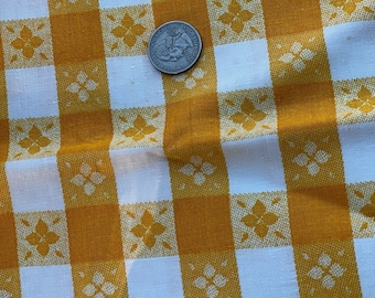 May include: Close-up of a vintage yellow and white checkered fabric with a floral pattern. A U.S. quarter coin rests on the fabric, providing a size reference. The fabric's design features alternating squares of yellow and white, with a repeating floral motif.