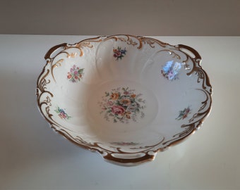 May include: A white porcelain bowl with gold trim and floral designs. The bowl has two handles and is perfect for serving fruit or snacks.