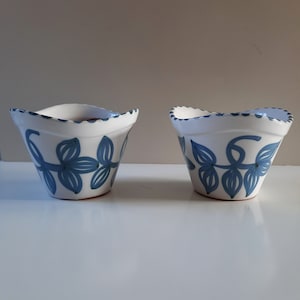 以下が含まれることがあります： 青い花柄の白いセラミックボウルが2つ。ボウルは波打った縁取りで、少し広がっています。