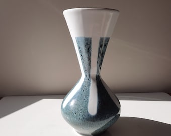 Könnte beinhalten: Eine weiße Keramikvase mit einer ausgestellten Öffnung und einem abgerundeten Körper. Die Vase hat ein blaues und weißes Streifenmuster mit einer gesprenkelten Textur.