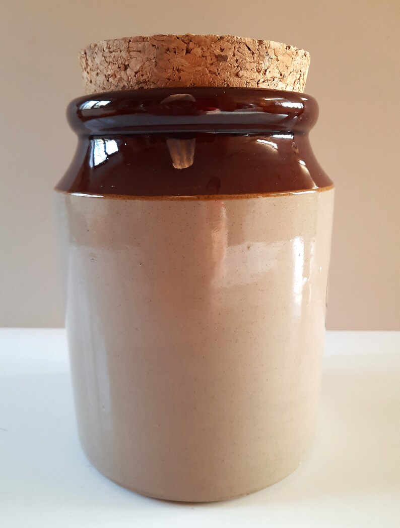 Peut inclure: Un pot en c&eacute;ramique brun et beige avec un couvercle en li&egrave;ge. Le pot est recouvert d'un glacis brun sur le dessus et le dessous et d'un glacis beige au milieu.