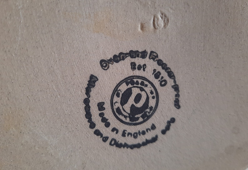Peut inclure: Un tampon circulaire noir et blanc avec le texte "Oven-fired Pottery - Proudly Made in England and Dishwasher Safe" et "Ref 18/10" au centre.