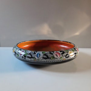 May include: A black ceramic bowl with a hand-painted floral design. The bowl has a wide rim and a rounded base. The floral design features colourful flowers and leaves on a white background.