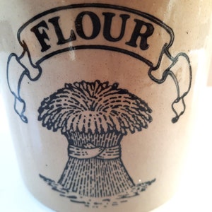 Peut inclure: Un r&eacute;cipient &agrave; farine en c&eacute;ramique vintage avec une illustration en noir et blanc d'une gerbe de bl&eacute; et le mot "FLOUR" dans une banni&egrave;re.