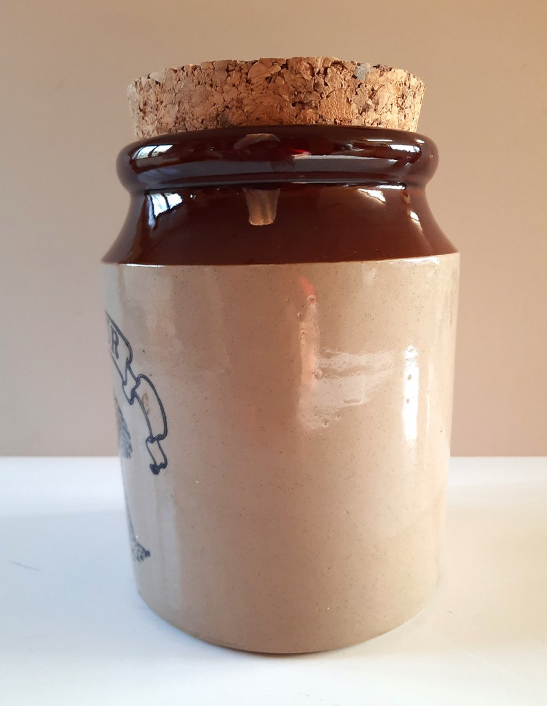 Peut inclure: Un pot en gr&egrave;s brun et beige avec un couvercle en li&egrave;ge. Le pot est recouvert d'un gla&ccedil;age brun sur le dessus et le dessous et d'un gla&ccedil;age beige sur le corps. Le pot a un design simple avec une petite image d&eacute;lav&eacute;e sur le c&ocirc;t&eacute;.