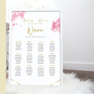 May include: A white wedding seating chart with gold accents and pink watercolor flowers. The chart lists the names of guests assigned to different tables. The text at the top reads "Abby & David, September 20, 2024, Welcome, Please Find Your Seat."