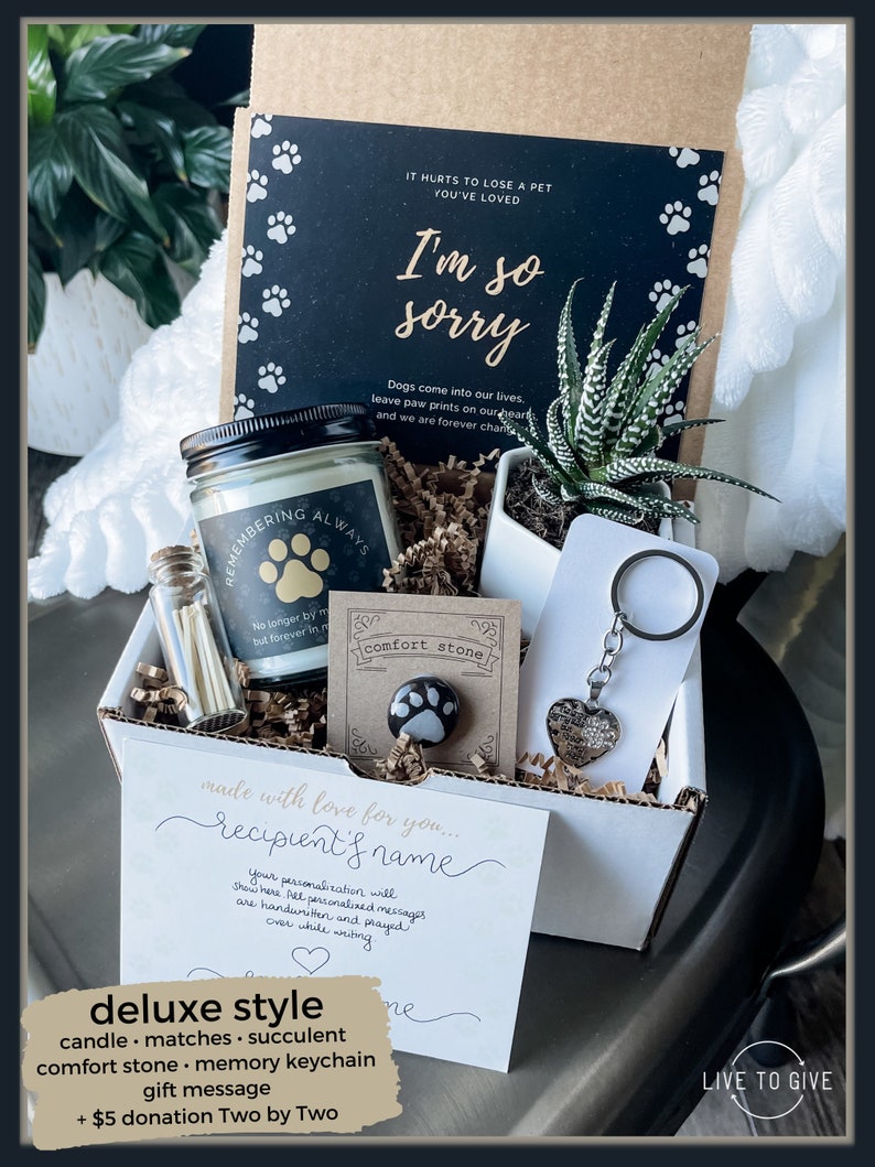 May include: A sympathy gift box with a white background and a black and white card that says "I'm so sorry". The box contains a candle, matches, a succulent, a comfort stone, a memory keychain, and a handwritten card. The box is labeled "Live to Give".