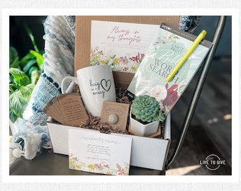 Könnte beinhalten: Eine Geschenkbox gefüllt mit Artikeln für ein nachdenkliches Geschenk. Die Box enthält eine weiße Tasse mit dem Text "hug in a mug", eine kleine Sukkulente im Topf, ein Buch mit dem Titel "Large Print Bible Word Search", einen gelben Stift und ein Kartenset mit inspirierenden Botschaften.