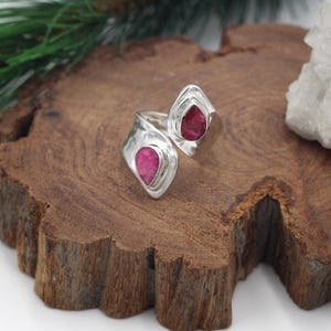 Może przedstawiać: Srebrny pierścionek z dwoma r&oacute;żowymi kamieniami szlachetnymi w kształcie łezki. Pierścionek ma młotkowaną fakturę i otwarty design. Kamienie są osadzone w oprawie, na drewnianej powierzchni.