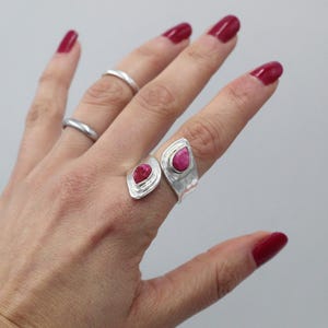 Może przedstawiać: Dłoń prezentuje trzy srebrne pierścionki, w tym dwa pierścionki z wyrazistymi, jaskrawoczerwonymi kamieniami szlachetnymi w kształcie łezki. Pierścionki mają młotkowaną fakturę. Paznokcie są pomalowane na pasujący czerwony kolor.