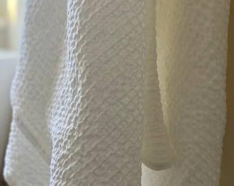 May include: White waffle weave bath towel hanging on a hook. The towel is soft and fluffy, with a textured surface.