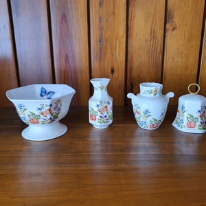 May include: A set of four white porcelain decorative pieces with floral and butterfly designs. The set includes a bowl, two vases, and a bell.