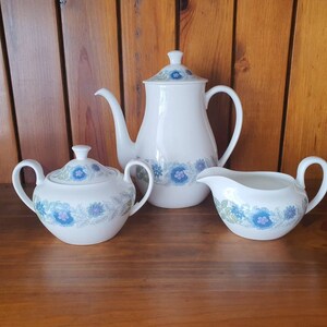 May include: A white teapot, sugar bowl, and creamer set with a blue and green floral pattern.