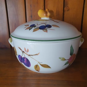 May include: White ceramic serving dish with a green rim and a lid. The lid has a yellow knob and a floral design with plums and leaves.