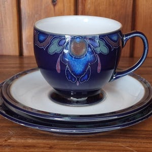 Könnte beinhalten: Ein blaues und weißes Tee-Set mit Blumenmuster. Die Tasse hat einen Henkel und einen breiten Rand. Die Untertasse hat einen gewellten Rand.