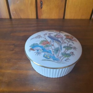 May include: A white porcelain trinket box with a gold trim and a floral design featuring blue and green birds and pink flowers.