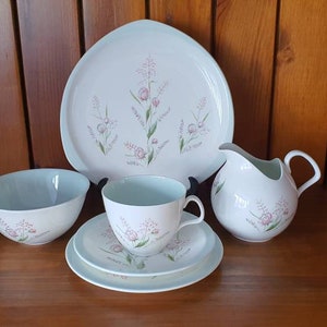 May include: A white tea set with a floral pattern. The set includes a teapot, a milk jug, a sugar bowl, a cup and saucer, and a serving plate.
