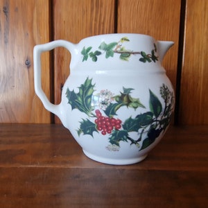May include: White ceramic pitcher with a floral design featuring holly, berries, and ivy. The pitcher has a rounded body and a handle.