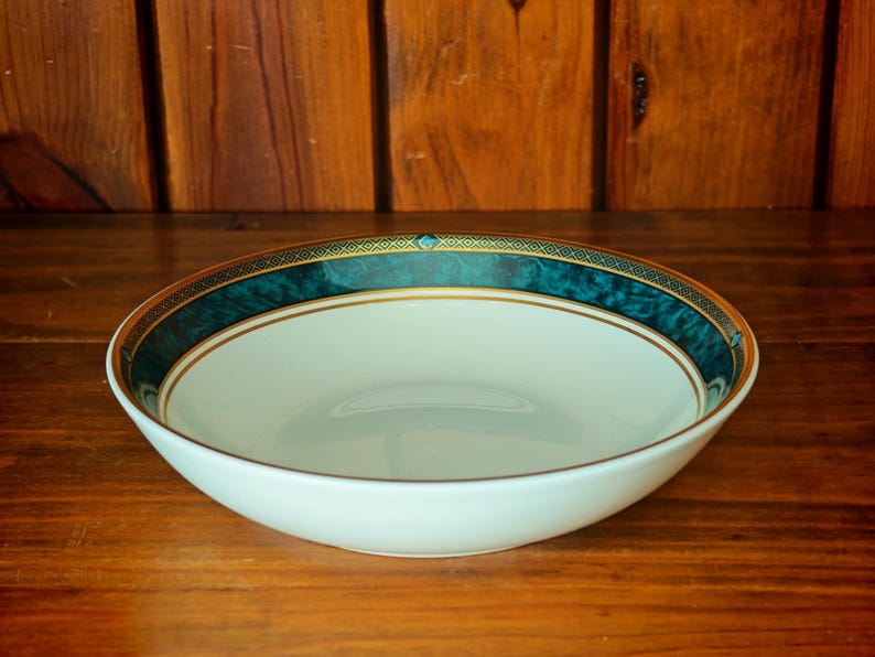 Peut inclure: Un saladier en c&eacute;ramique blanche avec une bordure d&eacute;corative turquoise et dor&eacute;e. Le bol est rond et pos&eacute; sur une surface en bois. La bordure turquoise a un effet marbr&eacute; et est orn&eacute;e d'une garniture dor&eacute;e.