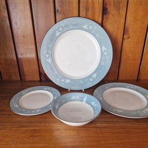 May include: A set of four blue and white ceramic plates with a floral design. The set includes a large dinner plate, two smaller plates, and a bowl.