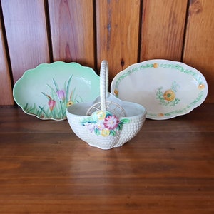May include: Three ceramic dishes with floral designs. A green oval dish with a floral design, a white oval dish with a floral design, and a white basket-shaped dish with a floral design.