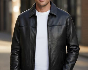 May include: A black leather jacket with a collared neckline and a front zip. The jacket is worn over a white t-shirt and paired with blue jeans. The person is standing outdoors with one hand in their pocket.