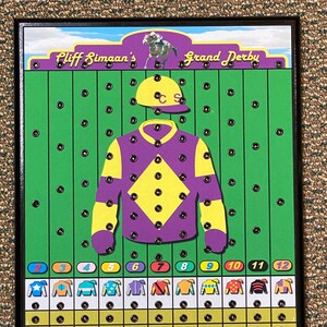 May include: A wooden game board with a green background and a purple jockey's uniform with yellow accents. The board has 12 numbered spaces and a horse racing theme. The text "Cliff Simaaan's Grand Derby" is at the top of the board.