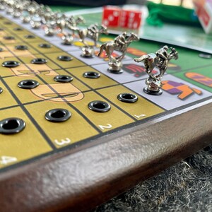 May include: A wooden game board with a yellow and green playing surface. The board has a brown wooden frame and black metal eyelets. There are silver horses with riders on the board. The numbers 1, 2, 3, and 4 are visible on the board.