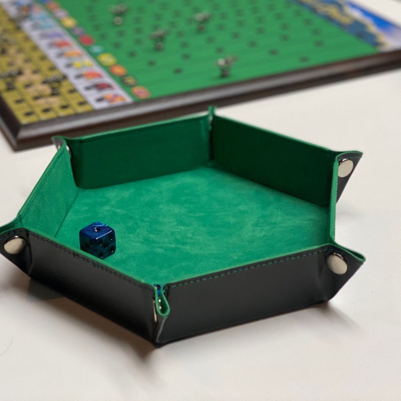 May include: A hexagonal dice tray with a green felt interior and black leather exterior. The tray has a blue dice inside.