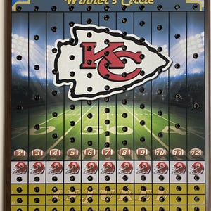 May include: A wooden game board with a football theme. The board features a red and white "KC" logo, a football field, and a grid of numbered holes. The text "Winner's Circle" is printed at the top of the board.