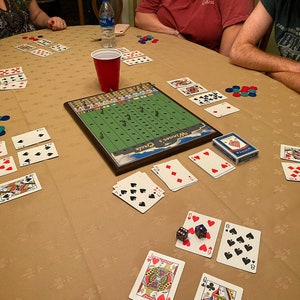 May include: A game of cards being played on a table with a green and brown game board in the center. The game board has the text "Off Limits" and "Pickle" on it. There are playing cards, chips, and dice on the table.