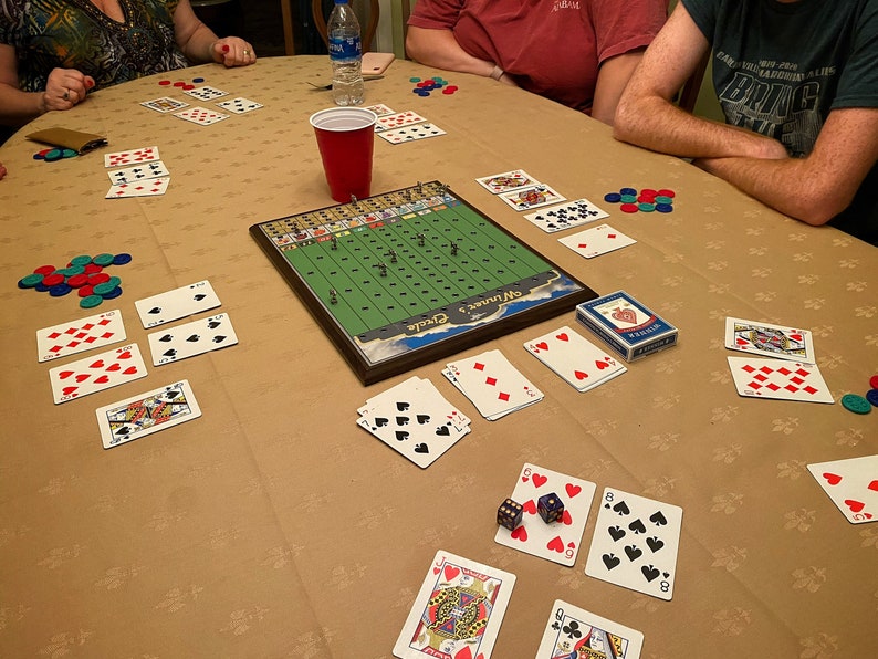 May include: A game of cards being played on a table with a green and brown game board in the center. The game board has the text "Off Limits" and "Pickle" on it. There are playing cards, chips, and dice on the table.