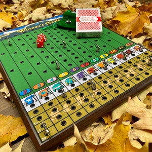 May include: A wooden game board with a green race track and colorful jockey silks. The game is called "Winner's Circle" and features a set of dice and small metal horses. The board is surrounded by fall leaves.