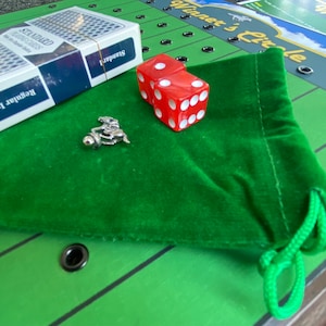 May include: A green felt bag with a drawstring, two red dice, a silver horse jockey figurine, and a deck of standard playing cards. The bag is on a green and black game board with the words "Winner's Circle" printed on it.