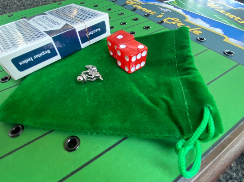 May include: A green felt bag with a drawstring, two red dice, a silver horse jockey figurine, and a deck of standard playing cards. The bag is on a green and black game board with the words "Winner's Circle" printed on it.