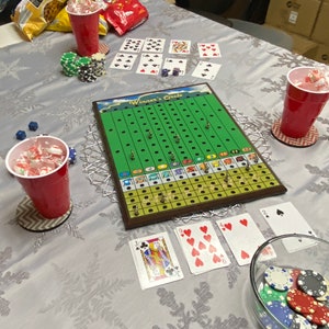 May include: A green and brown board game called "Winner's Circle" with playing cards and chips on a white tablecloth. The game board has a green track with numbered spaces and a red, white, and blue color scheme.