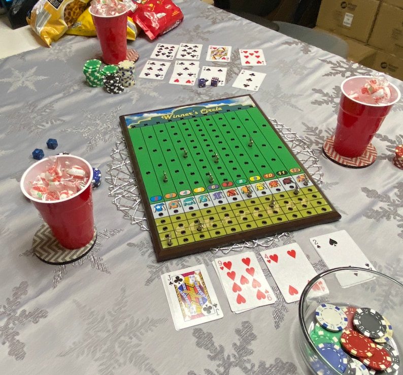 May include: A green and brown board game called "Winner's Circle" with playing cards and chips on a white tablecloth. The game board has a green track with numbered spaces and a red, white, and blue color scheme.