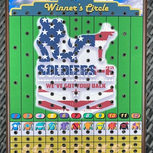 May include: A wooden game board with a green field and a yellow track. The board features a patriotic design with a soldier and a dog, and the text "SOLDIERS-6 WE'VE GOT YOUR BACK". The board has a grid of holes and a row of numbered spaces at the bottom.