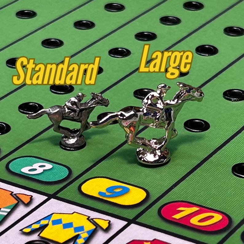 May include: Two silver horse racing game pieces, one labeled "Standard" and the other "Large". The pieces are on a green game board with black holes and numbered spaces.