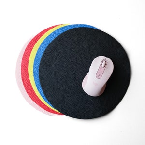 May include: A set of five round leather mouse pads in pink, red, yellow, blue, and black. The black mouse pad has a pink wireless mouse on top.