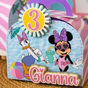 May include: A personalized party favor box featuring Daisy Duck and Minnie Mouse in a beach scene. The box has a purple handle and a sun-shaped number 3. The name "Gianna" is displayed in pink letters.