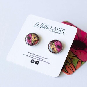 Op de afbeelding: Een paar ronde oorstekers met een bloemenpatroon in roze, geel en wit. De oorbellen zijn gezet in zilverkleurig metaal en worden gepresenteerd op een witte kaart met de tekst "White Label Earrings".